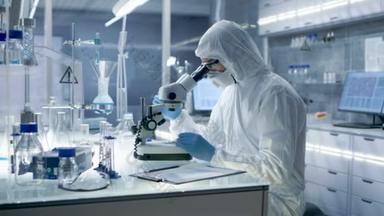 穿防护<strong>服</strong>的人员在实验室用显微镜观察并记录